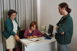 A ex-entrevistada do Vale Registrar, Anna Amélia Lopes de Oliveira, assina o Termo de Doação, ao lado da Assessora Técnica e do Gerente Operacional do Núcleo de História Oral, Josanne Simões e Eder Melo, na Sala de Histórias, da Estação Ferroviária de Ouro Preto. Foto: Rafael Santos