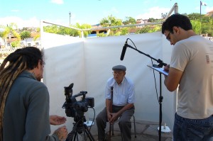 – Marcello Nicolato, auxiliado por Rafael Bouças, do Núcleo de Audiovisual do Vale Registrar, grava o depoimento de Varleno Benedio Ferreira, dentro da cabine de depoimentos, em frente ao Centro de Convenções. Foto: Dalila Carneiro 