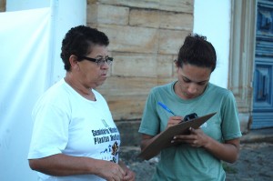 Cristiane Evangelista preenche os dados pessoais do Termo de Autorização para uso de imagem da depoente Ana Maria de Lima Pinto, no adro da Igreja Nossa Senhora do Rosário dos Pretos, no bairro Rosário, em Mariana. Foto: Marianne Fonseca